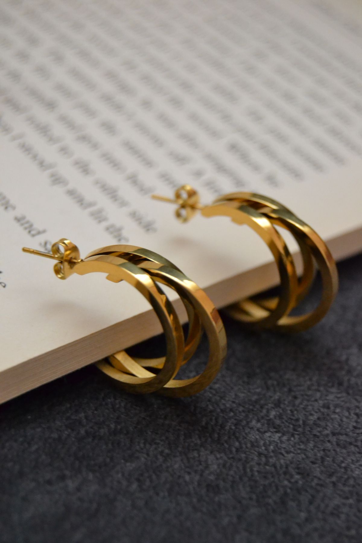 Goldene Creolen mit doppeltem Ringdesign liegen auf einer aufgeschlagenen Buchseite