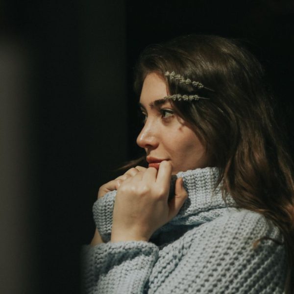 Frau mit langen Haaren und Haarschmuck trägt grob gestrickten Pullover und schaut nach rechts